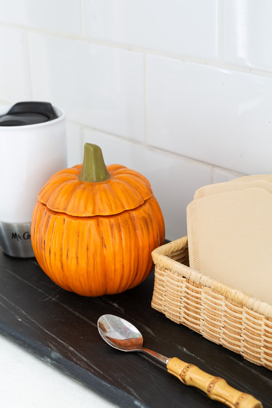 orange ceramic pumpkin bowl with lid to hold sugar for the fall season placed on a kitchen counter coffee station.